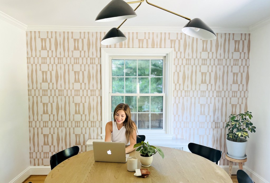 woman sitting at table with laptop and geometric accent wall in background