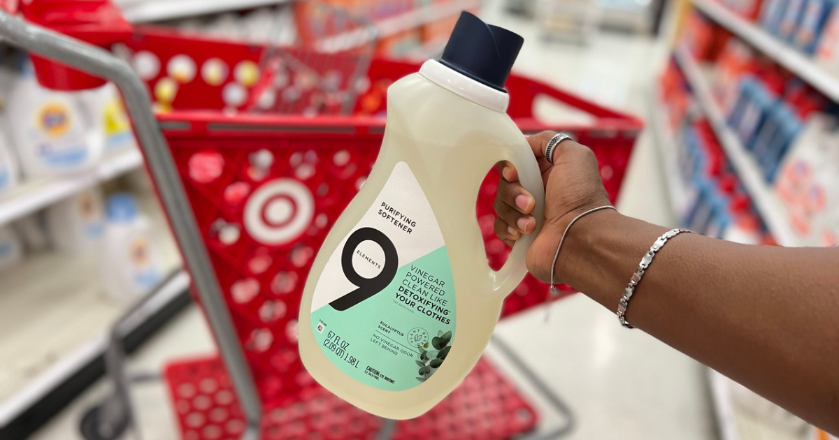 hand holding a bottle of 9 Elements Liquid Purifying Softener in front of a Target cart