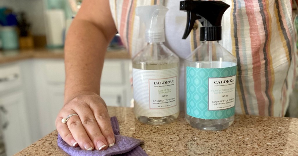 woman wiping countertop and two spray bottle of cleaner