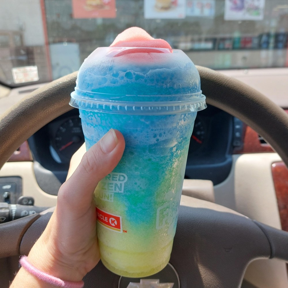 hand holding a Circle K Froster in front of a steering wheel