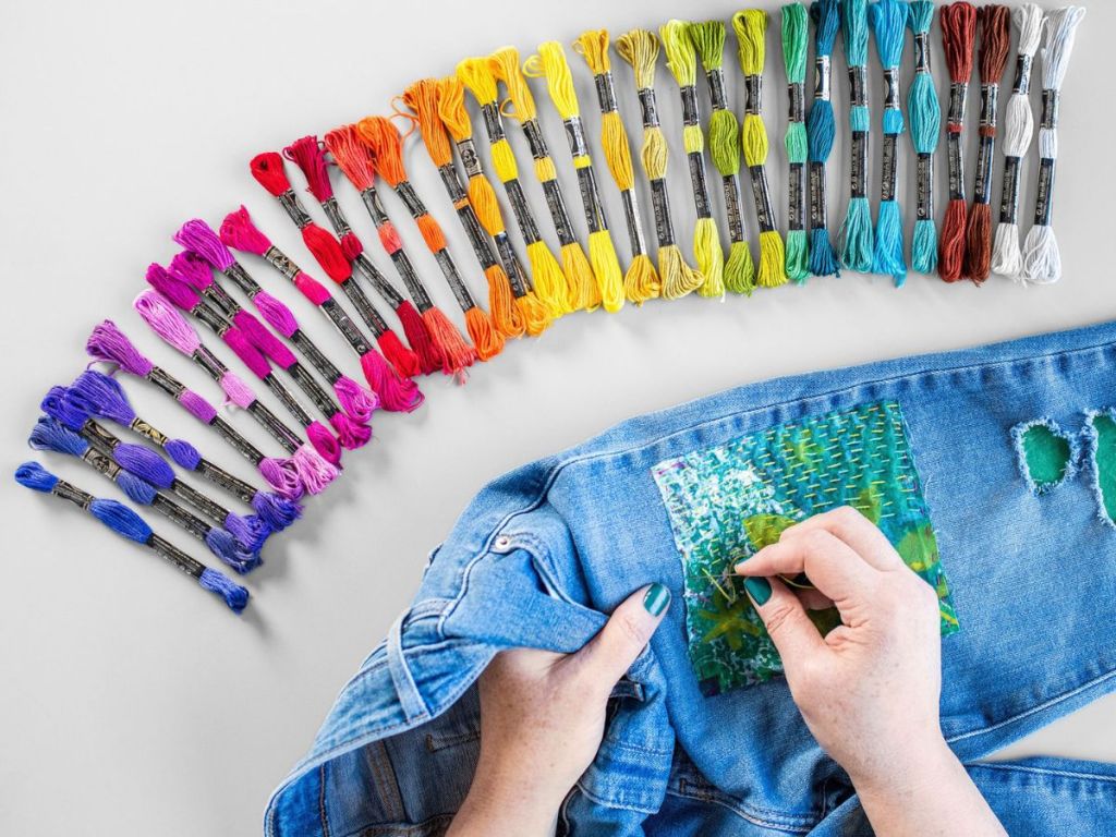 person embroidering jeans with lots of colors of embroidery floss in front of them