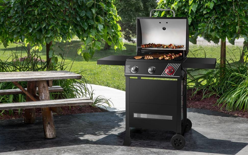 Grill with the lid open and food on it next to a picnic table
