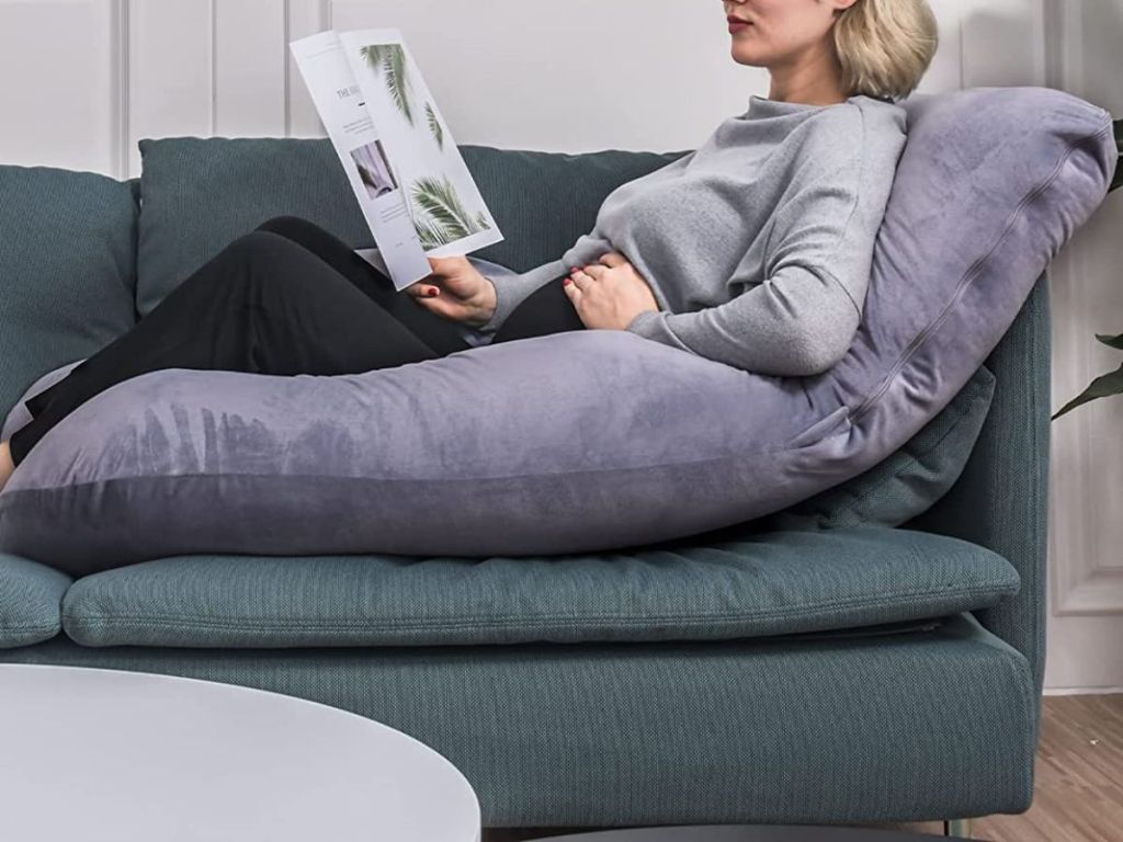 woman reading a book while laying on u-shaped body pillow on the couch