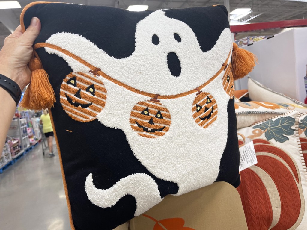 ghost holding a string of pumpkin garland on a throw pillow