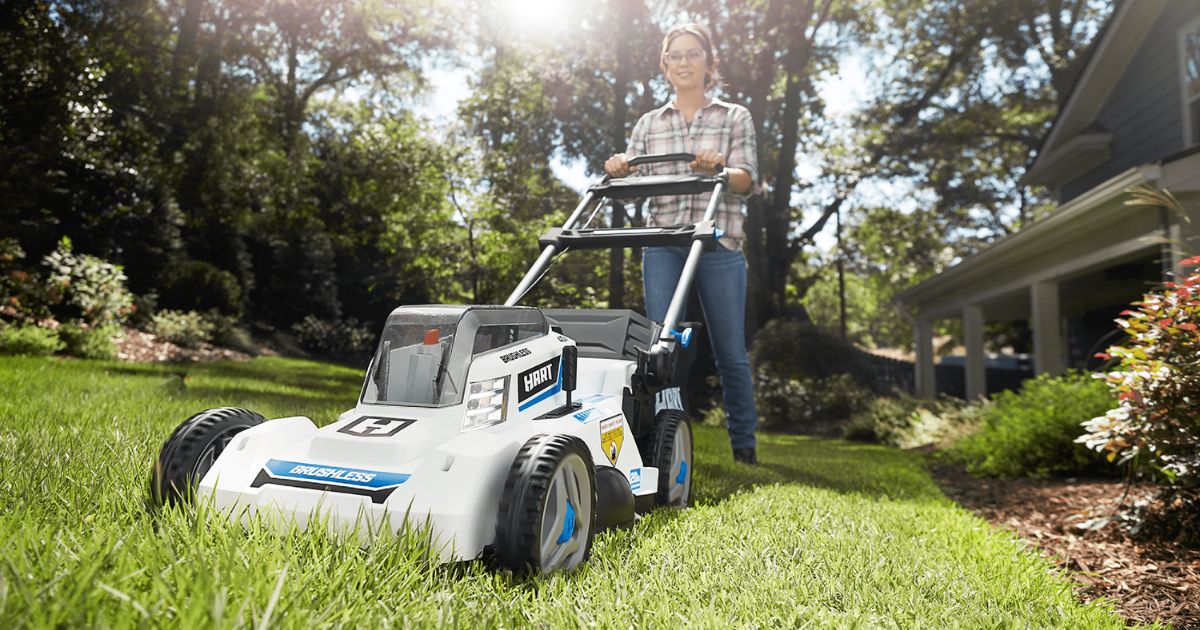 brushless cordless Hart lawn Mower being pushed on gras by a woman wearing jeans and a plaid shirt