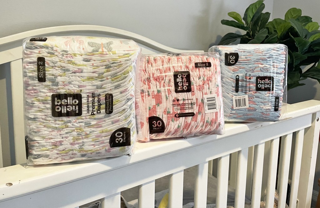 three packs of hello bello diapers on edge of crib