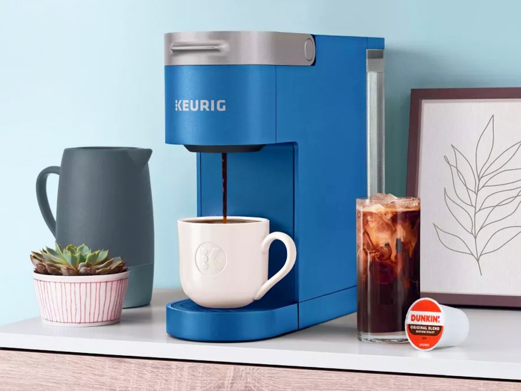 blue keurig machine brewing cup of hot coffee with iced coffee next to it