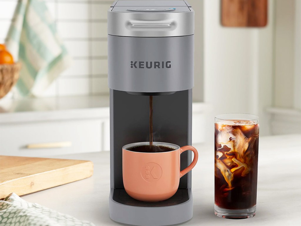 grey keurig machine brewing cup of hot coffee next to cup of iced coffee