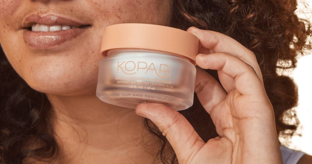 Lady holding Kopari lotion next to her face