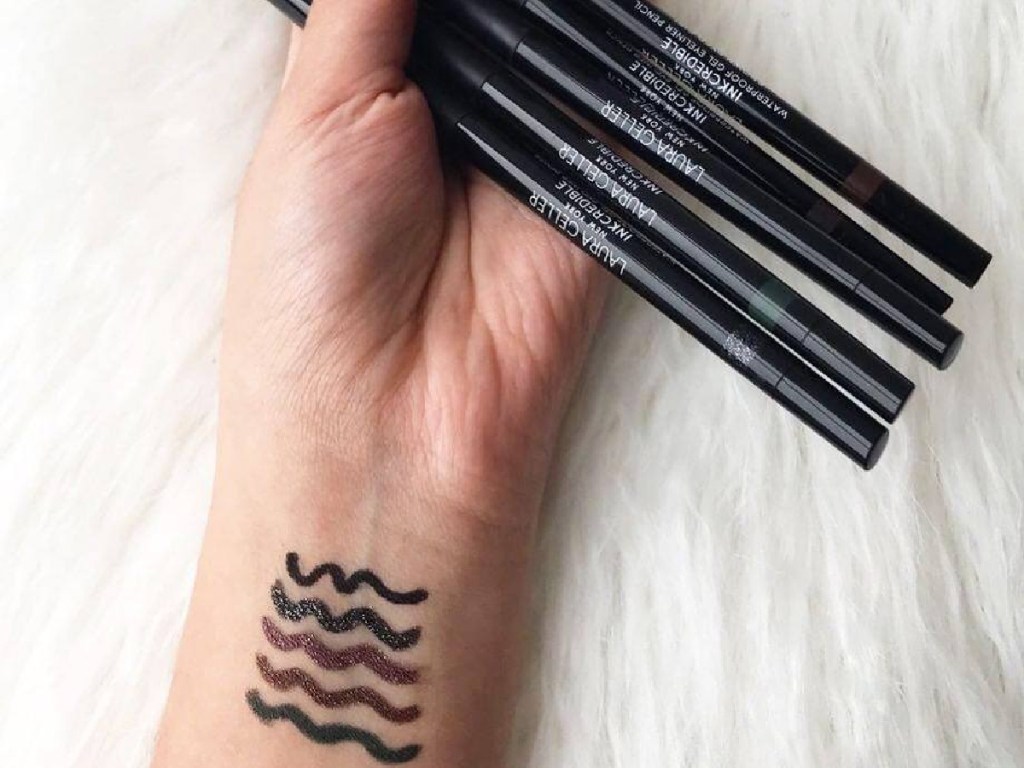 woman's hand holding five eyeliners with swatches on wrist