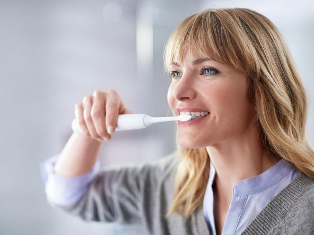 woman brushing her teeth using an electric toothbrush