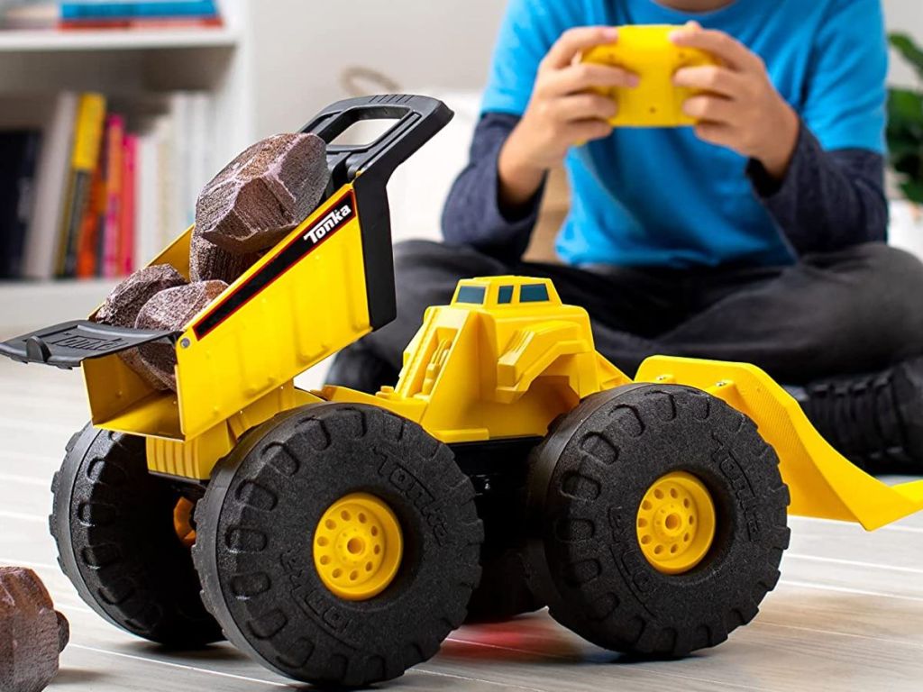 A child using a remote to control a Yellow Tonka Dump Truck