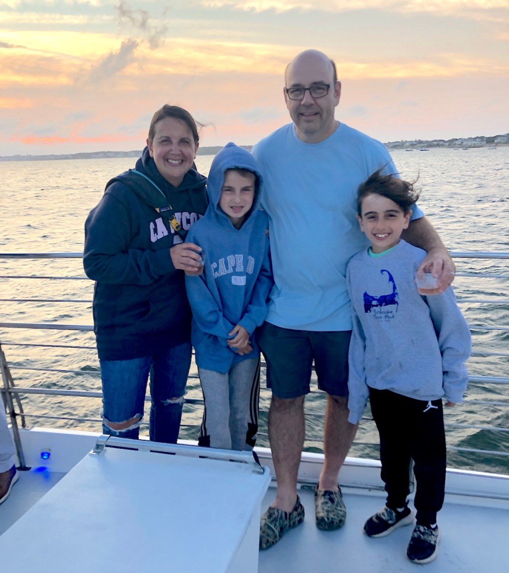 family standing together wearing cape cod sweatshirts by water and sunset