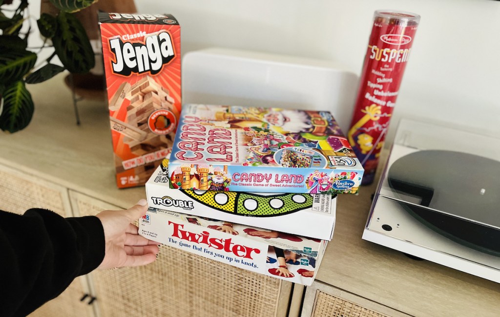 hand holding pile of board games for kids on console table