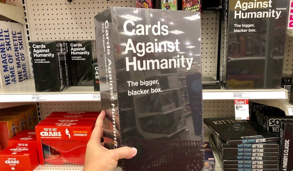 hand holding bigger blacker box of cards against humanity board game for adults