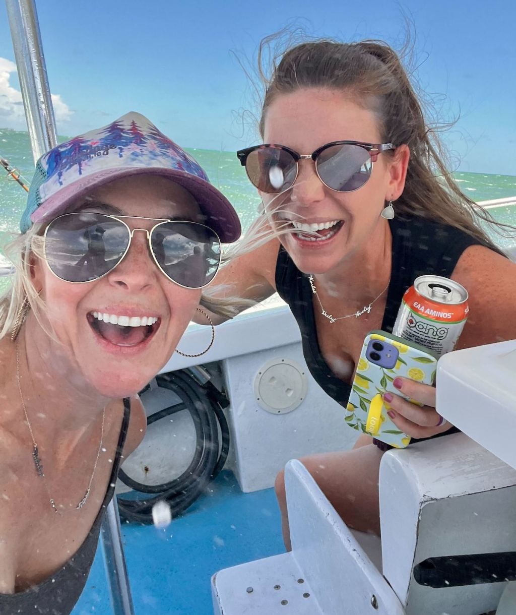 two women wearing sunglasses smiling on boat in ocean blue waters