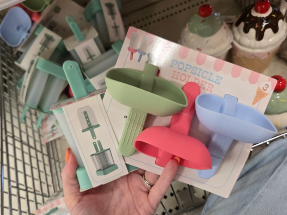 A hand holds a package of colorful popsicle holders in green, red, and blue, labeled