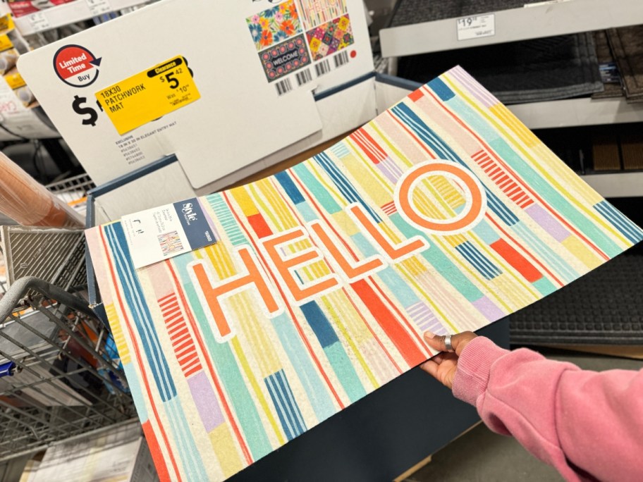 hand reaching for a colorful doormat with the word "Hello" in a store display bin