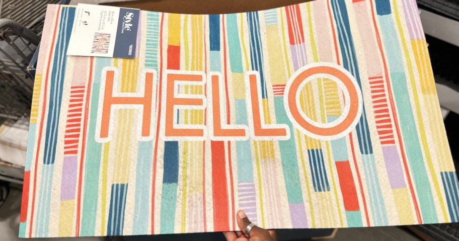 hand reaching for a colorful doormat with the word "Hello"