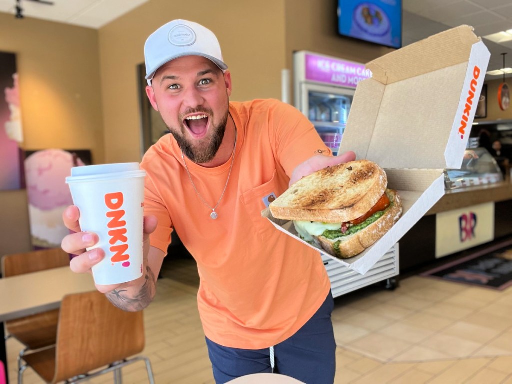 man holding coffee and grilled cheese pesto sandwich at dunkin