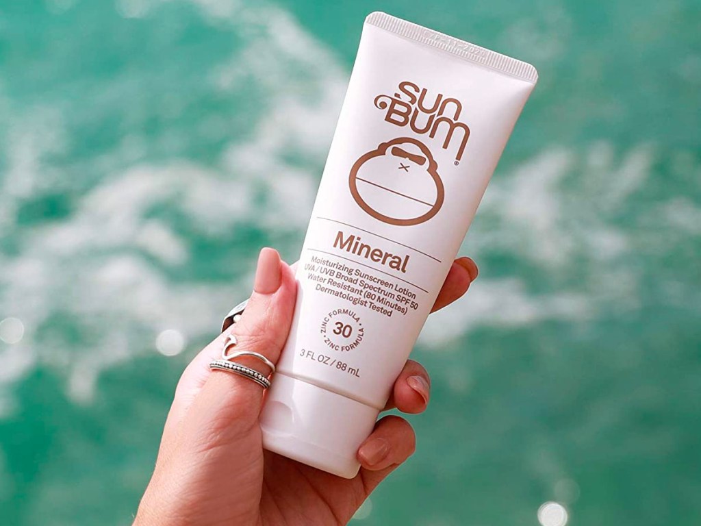 hand holding sun bum mineral sunscreen over water