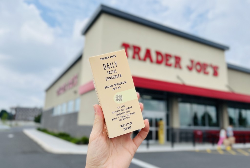 hand holding trader joe's daily facial sunscreen in front of store front