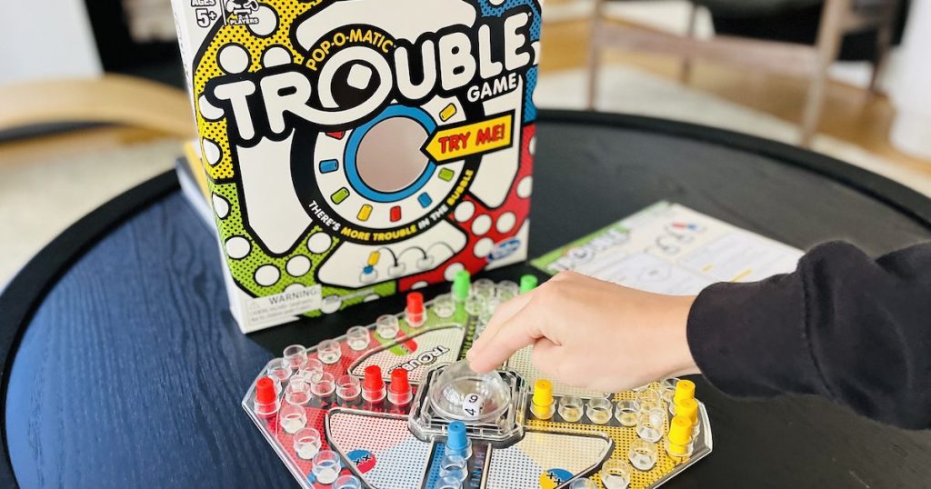 trouble board game for kids set up on black coffee table and hand pushing on bubble