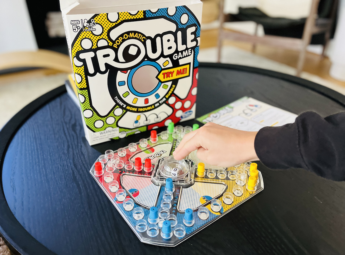 trouble board game for kids set up on black coffee table and hand pushing on bubble