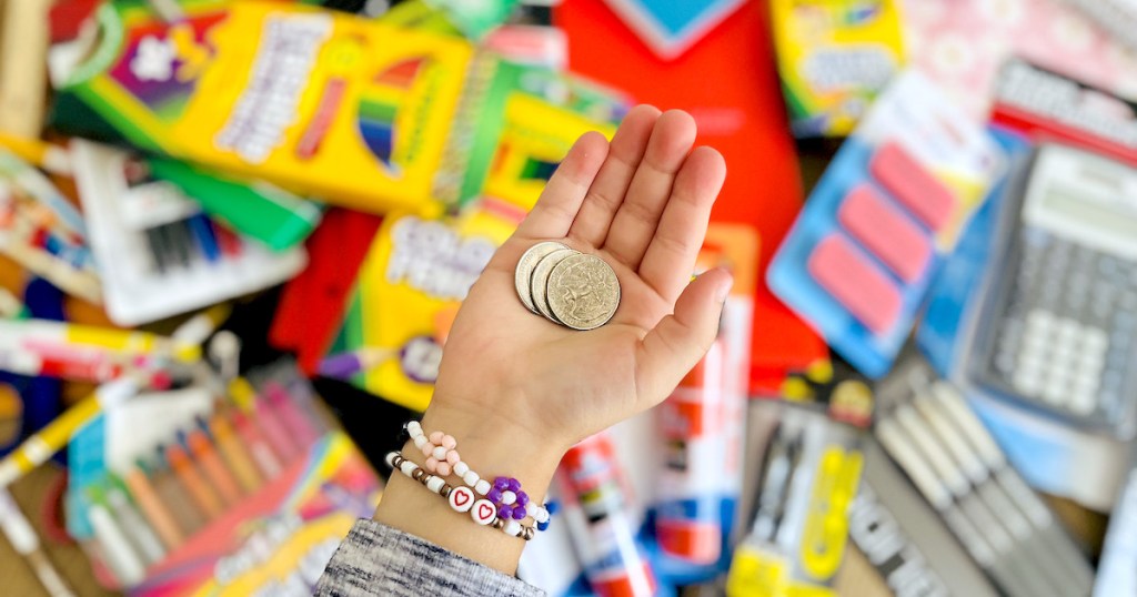 hand holding quarters over pile of school supplies