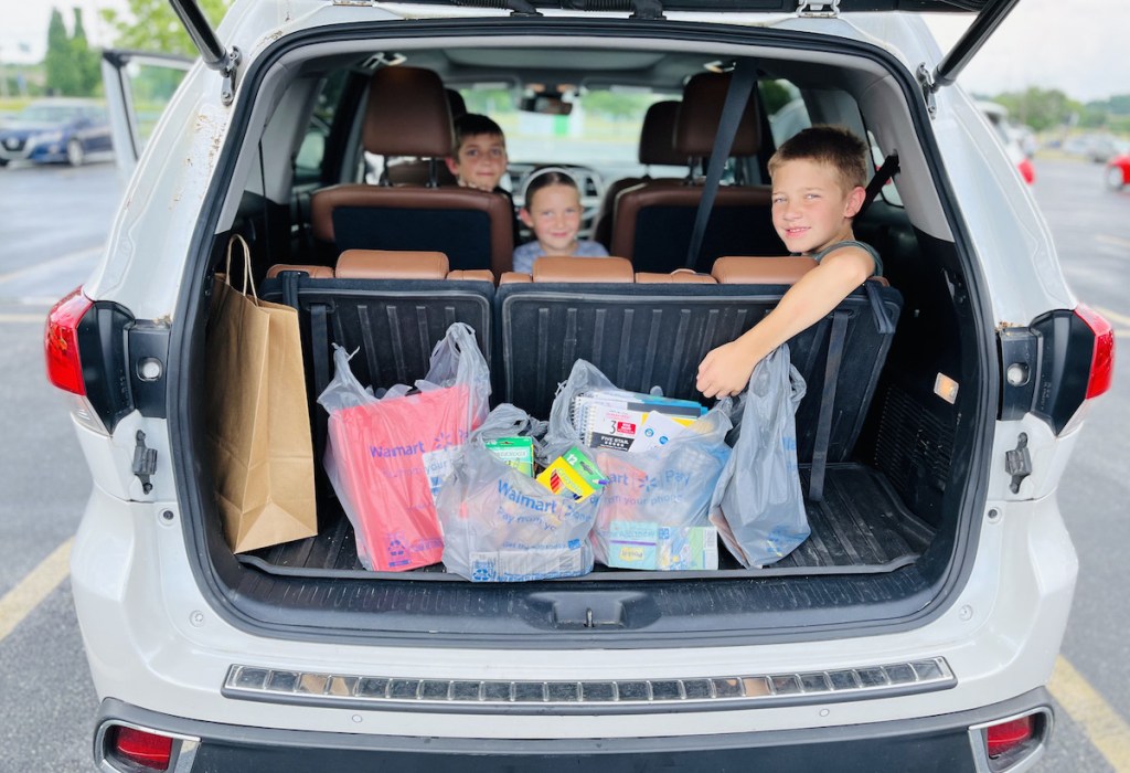 kids sitting in car with open trunk and walmart store pick up bags