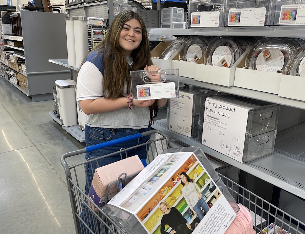 girl standing in walmart aisle holding clear organizers for dorm room ideas and essentials