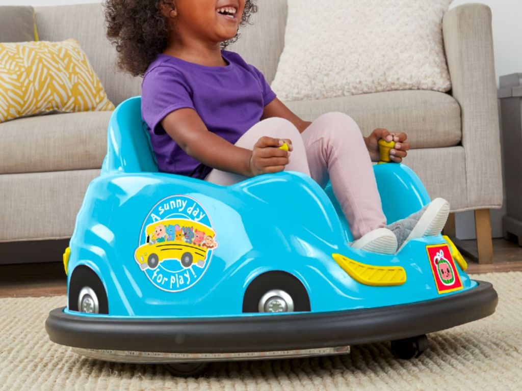 a little boy riding a CoComelon 6V Bumper Car in a living room