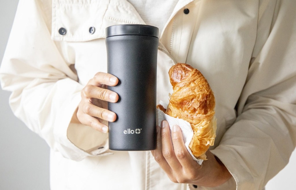 person holding a coffee tumbler and croissant