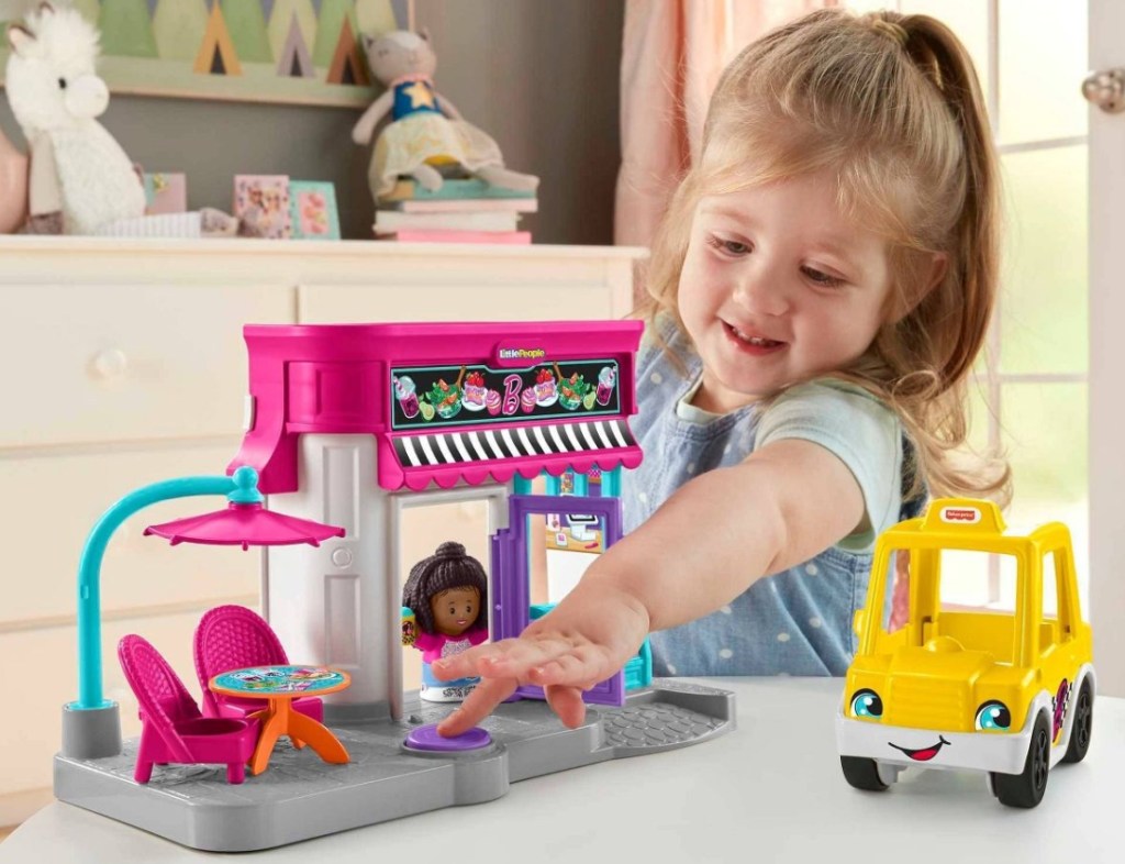 girl playing with a Fisher-Price Little People Barbie City Adventures Cafe and Cab Playset