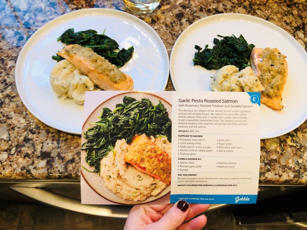 hand holding a recipe card by two plates of food
