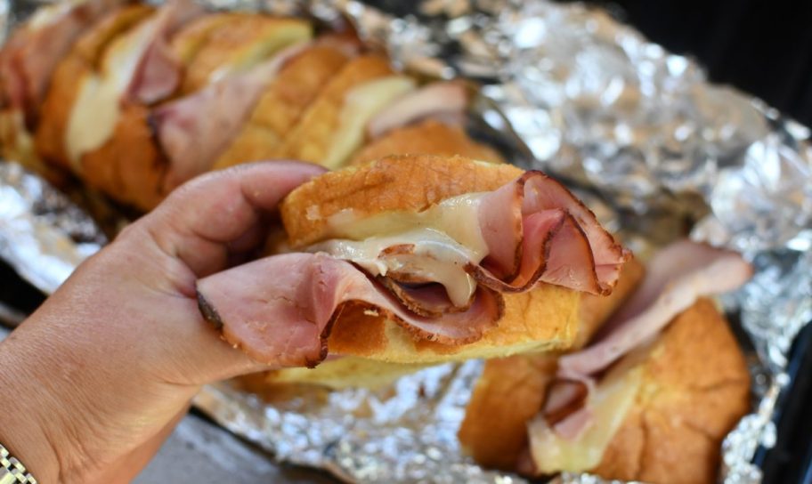 hand holding up Grilled Ham and Cheese Pull Apart Sandwiches made on the grill, one of our favorite camping food ideas and tailgaiting recipes