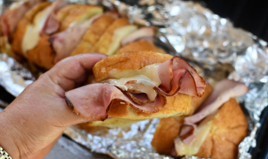 hand holding up Grilled Ham and Cheese Pull Apart Sandwiches made on the grill, one of our favorite camping food ideas and tailgaiting recipes
