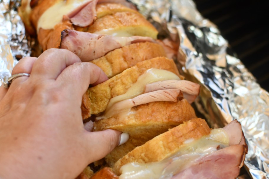Hand grabbing ham and grilled cheese pull apart sandwiches from the grill