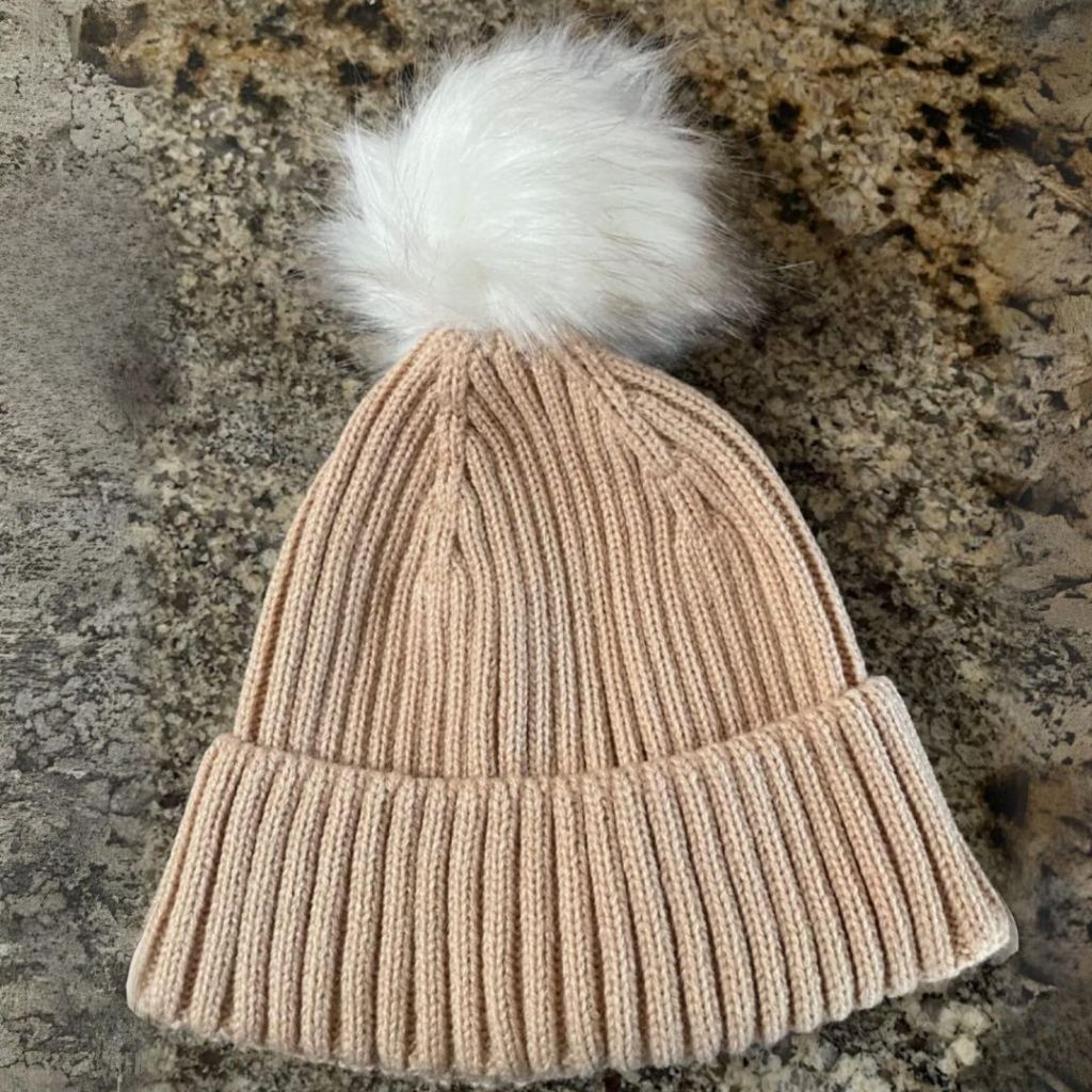 tan ribbed women's beanie with white fur pom on counter