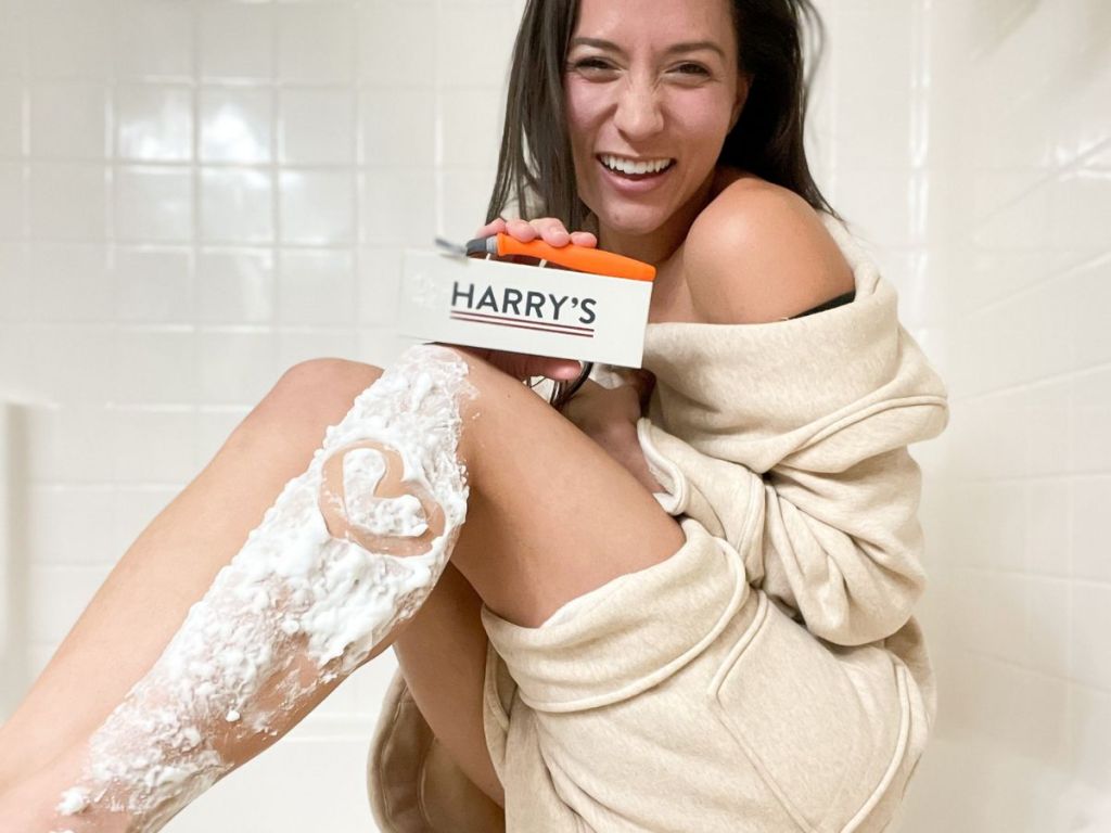 woman holding a Harry's razor and box with shaving cream on her leg and a heart drawn in the shaving cream