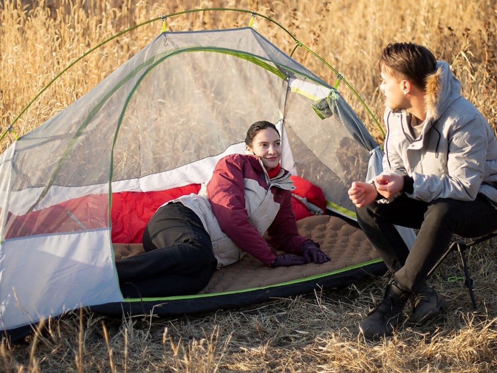 woman laying on air mattress inside tent and man sitting in camping chair outside