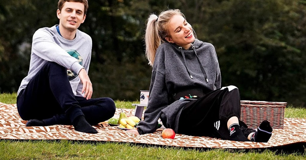 man and woman sitting on outdoor blanket in park