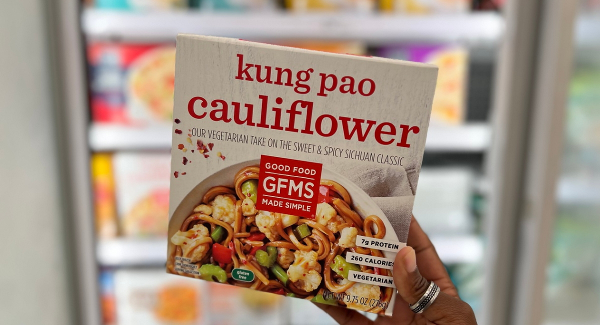 hand holding up a good food made simple Kung Pao Cauliflower Meal in front of a store freezer case
