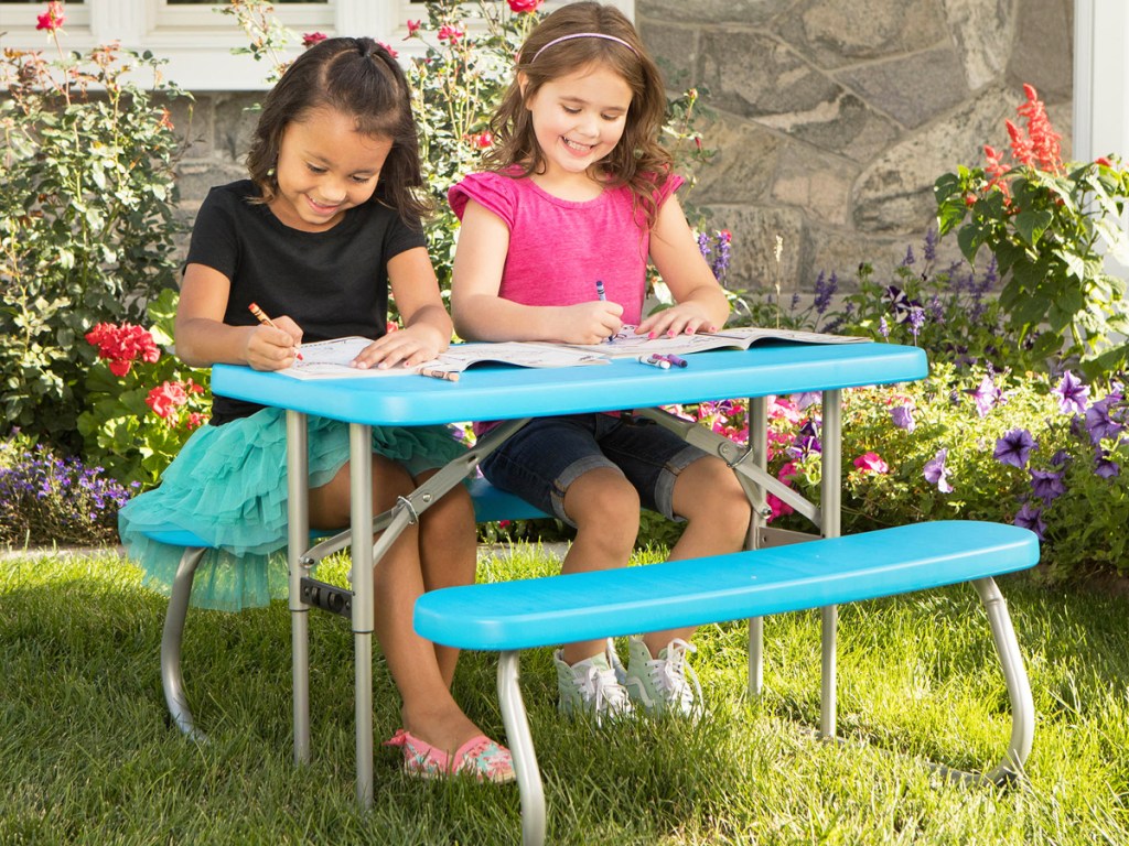 two girls coloring outside on a blue picnic table