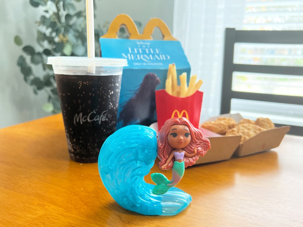 little mermaid toy in front of happy meal and drink