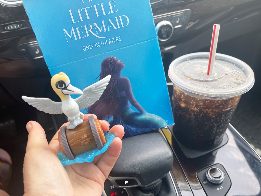 hand holding a little mermaid toy near happy meal box and drink
