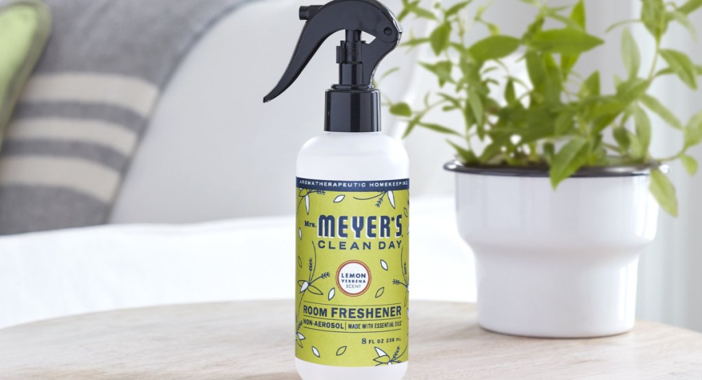 Mrs. Meyer's Room and Air Freshener Spray 8oz Bottle in Lemon Verbena on table with plant behind it