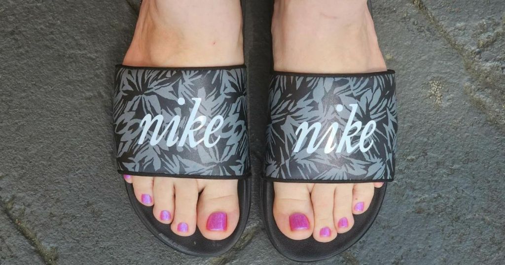A woman with pink toenails wearing Nike Slides