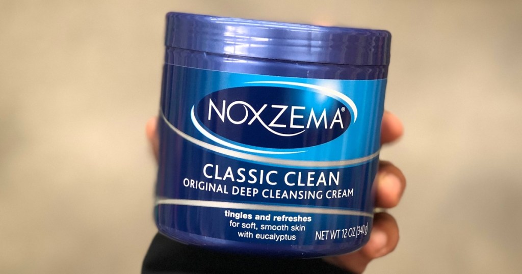 hand holding a blue jar of Noxzema cleanser