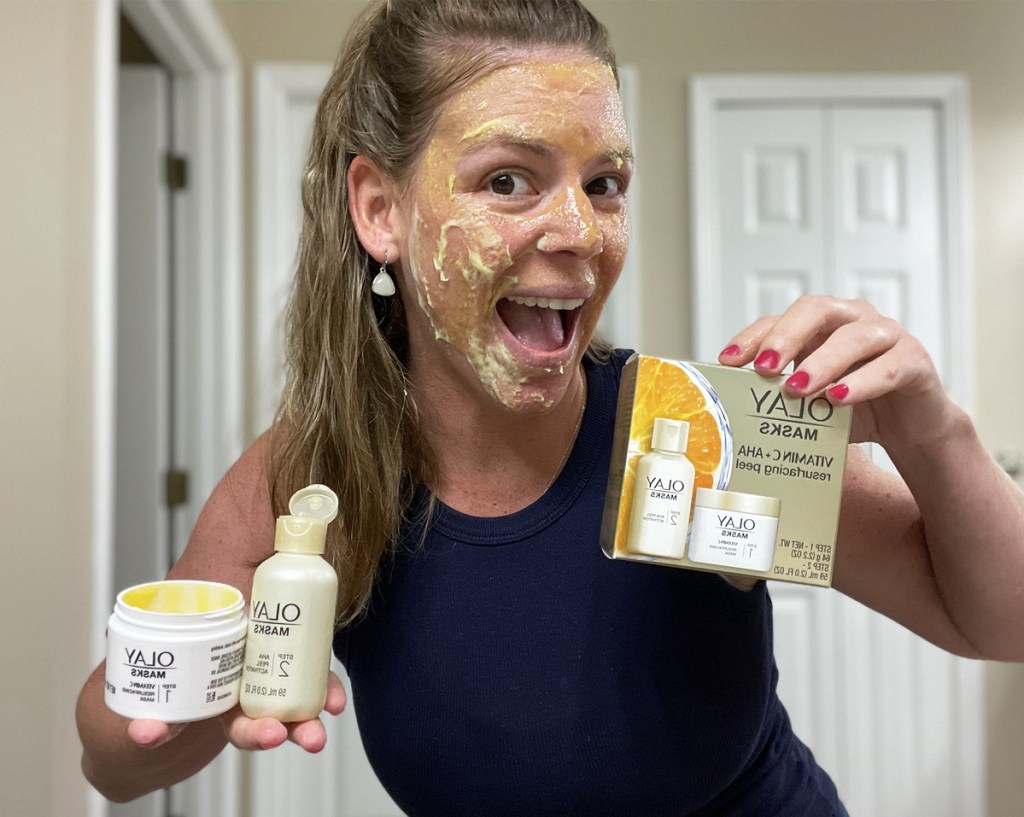 woman with olay mask on her face holding up the box and products